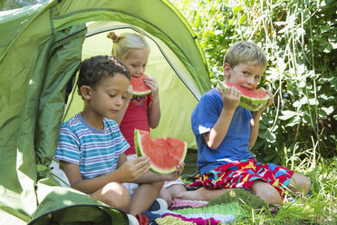 Drei Kinder essen Wassermelonenscheiben im Gartenzelt - CUF35277