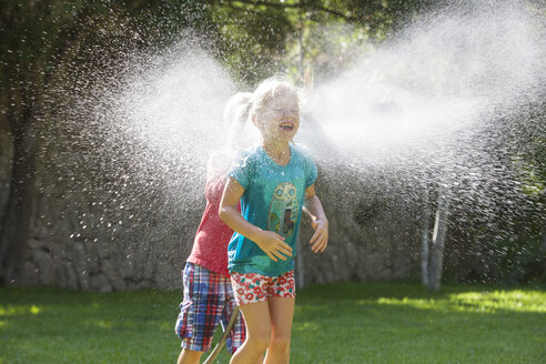 Junge jagt Mädchen im Garten mit Wassersprinkler - CUF35283