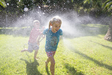 Junge läuft Mädchen im Garten mit Wassersprenger hinterher - CUF35284