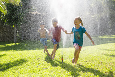 Drei Kinder im Garten, die durch einen Wassersprinkler laufen - CUF35285