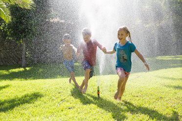 Three children in garden running through water sprinkler - CUF35285