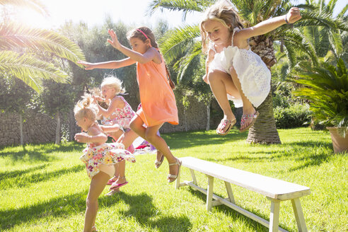 Fünf energiegeladene Mädchen springen von der Gartenbank - CUF35325