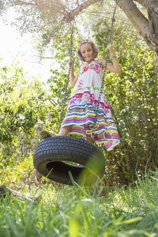 Porträt eines Mädchens, das auf einer Baumschaukel im Garten schwingt, lizenzfreies Stockfoto