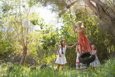 Vier Mädchen spielen auf einer Baumreifenschaukel im Garten - CUF35341