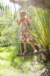 Girl standing swinging on tree swing in garden - CUF35348