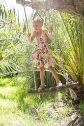 Mädchen stehend schwingend auf Baumschaukel im Garten - CUF35348