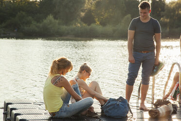 Drei junge erwachsene Freunde binden Schnürsenkel am Flussufer - CUF35362