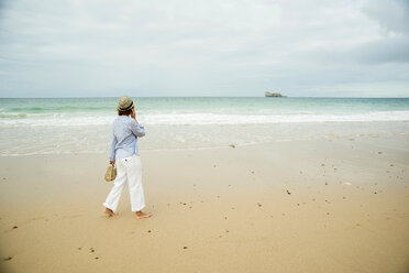 Ältere Frau, die am Strand spazieren geht und mit ihrem Smartphone chattet, Camaret-sur-mer, Bretagne, Frankreich - CUF35371