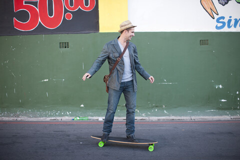 Mittlerer Erwachsener, männlich, der auf einer Straße Skateboard fährt, lizenzfreies Stockfoto