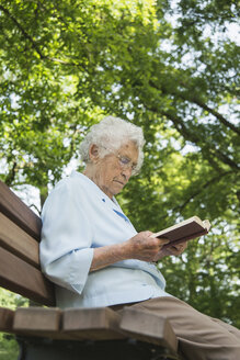 Ältere Frau sitzt auf einer Parkbank und liest in der Bibel - CUF35459