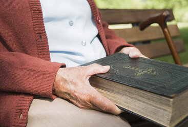 Mid section of senior woman, sitting on park bench, holding bible - CUF35462