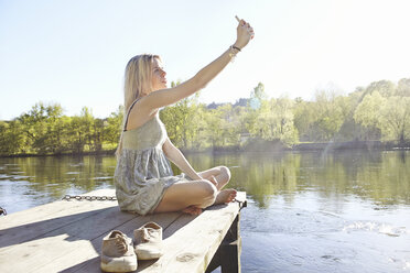 Young woman sitting on jetty photographing herself - CUF35497
