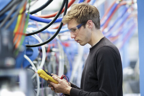 Mittlerer erwachsener männlicher Techniker, der Kabel in einer technischen Anlage prüft - CUF35508