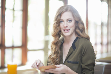 Young woman sitting at restaurant table with slice of toast - CUF35698