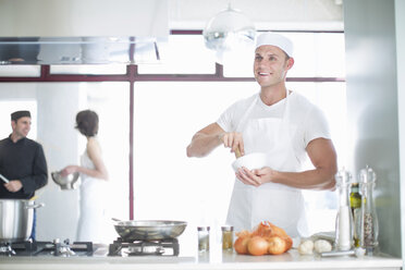 Porträt eines lächelnden männlichen Kochs, der mit Mörser und Stößel in einer Großküche mischt - CUF35701