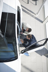 Overhead view of salesman and customer inspecting new car in car dealership - CUF35730