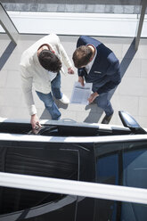 Overhead view of salesman and customer looking at new car in car dealership - CUF35731