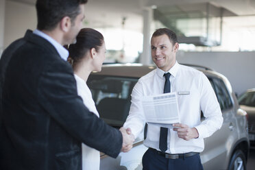 Mid adult couple making deal with salesman in car dealership - CUF35733