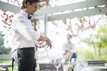 Kellner bereitet Weingläser auf einem Tisch in einem Terrassenrestaurant vor - CUF35767