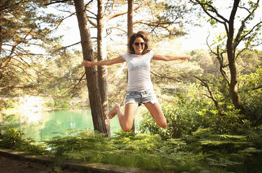 Mid adult woman jumping mid air, Blue Pool, Wareham, Dorset, UK - CUF35788