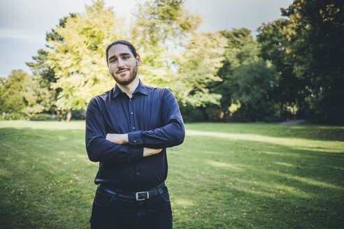 Young businessman standing in park with arms crossed - JSCF00104