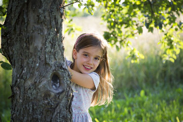 Young girl behind tree trunk at summer evening - LVF07164