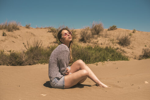 Spanien, junge Frau mit Sonnenbrille, die am Strand sitzt und sich entspannt - ACPF00051
