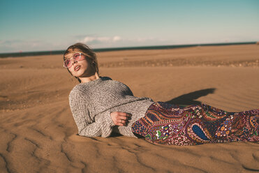 Spanien, modische junge Frau mit Sonnenbrille am Strand liegend - ACPF00052