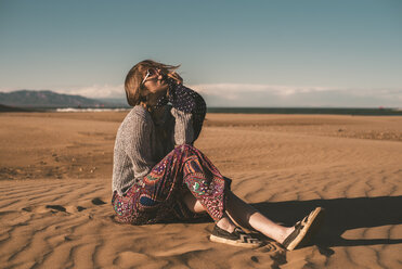 Spain, fashionable young woman wearing sunglasses sitting on the beach - ACPF00053