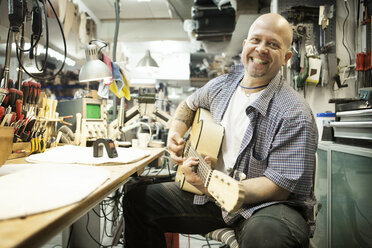 Porträt eines Gitarrenbauers, der eine akustische Gitarre in der Werkstatt stimmt - CUF35908