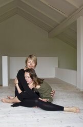 Mutter und zwölf Jahre alte Tochter umarmen sich auf dem Boden - CUF36216