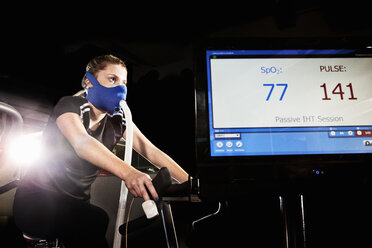 Young woman in face mask on gym exercise cycle in altitude centre - CUF36220