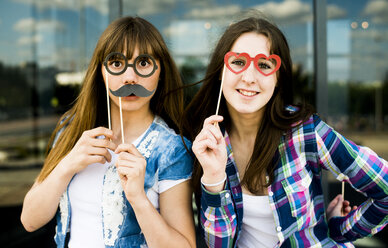 Porträt von zwei jungen Frauen, die Schnurrbart- und Brillenkostüm-Masken hochhalten - CUF36264