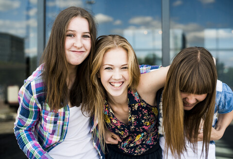 Porträt von drei jungen Frauen, die vor einem gläsernen Bürogebäude lachen, lizenzfreies Stockfoto