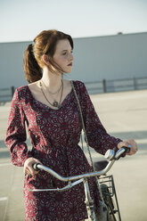 Junge Frau schiebt ihr Fahrrad auf einem leeren Parkplatz - CUF36289