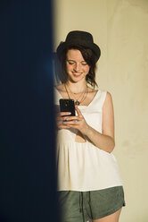 Young woman leaning against wall reading text on smartphone - CUF36292