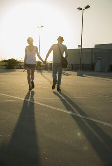 Romantisches junges Paar schlendert Hand in Hand über einen leeren Parkplatz - CUF36293
