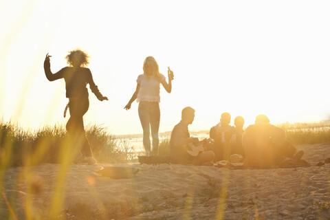 Sechs erwachsene Freunde feiern bei Sonnenuntergang am Strand von Bournemouth, Dorset, Großbritannien, lizenzfreies Stockfoto