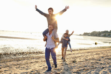 Men giving piggyback ride to women on beach - CUF36359