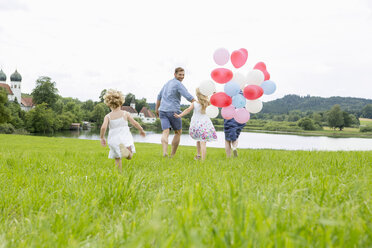 Family running through field with balloons - CUF36407