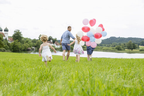 Familie läuft mit Luftballons durch ein Feld - CUF36407