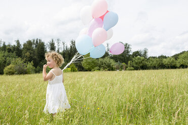 Young girl holding balloons in field - CUF36419