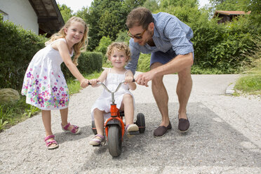 Mädchen fährt Dreirad mit Vater und Schwester - CUF36422