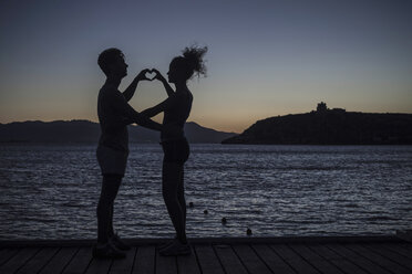 Couple making heart shape with hands by sea, silhouette - CUF36453