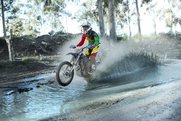 Junger männlicher Motocross-Fahrer, der durch einen Waldfluss spritzt - CUF36513