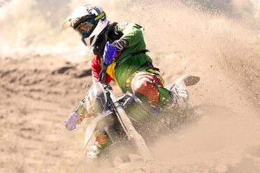 Young male motocross rider racing and leaning into mud track - CUF36514