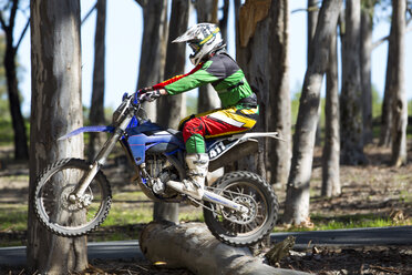 Junger männlicher Motocross-Fahrer, der auf einen Baumstamm springt - CUF36515
