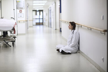 Ärztin sitzt im Schneidersitz im Krankenhausflur - CUF36538