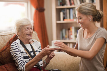 Pflegeassistentin reicht einer älteren Frau eine Kaffeetasse - CUF36590
