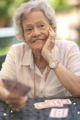 Ältere Frau spielt Karten am Gartentisch - CUF36604